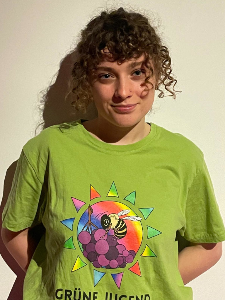 Portraitfotografie von Jule Schaible vor einem weißen Hintergrund. Trägt das Grüne Jugend Rems-Murr T-Shirt.