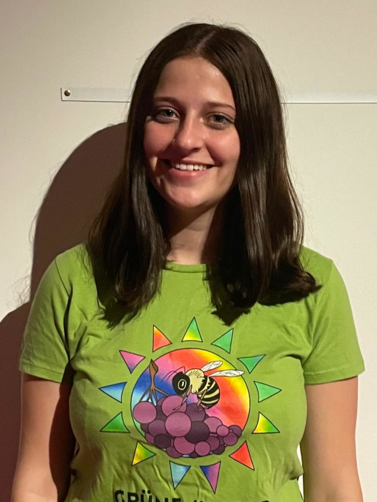 Portraitfotografie von Sara Schmalzried vor einem weißen Hintergrund. Trägt das Grüne Jugend Rems-Murr T-Shirt.